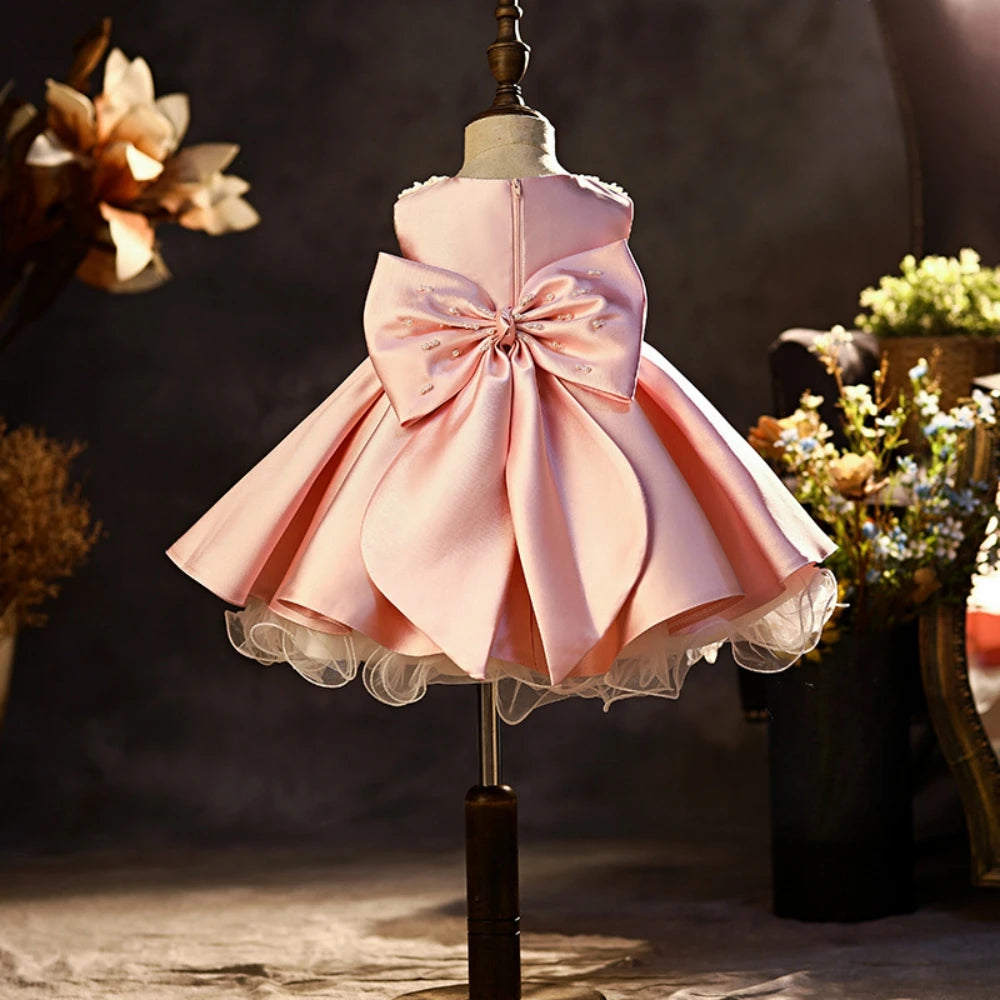 Pink satin princess girl’s dress with glitter pearls, sleeveless design, pink bow, suitable for school performances and catwalk shows.