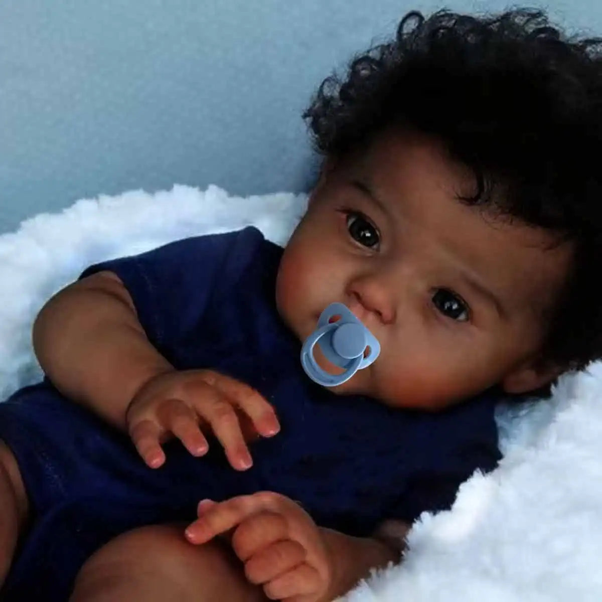 Black Reborn baby doll by Ansoff with soft cloth body, curly hair, and realistic newborn features, perfect for collectors or play.
