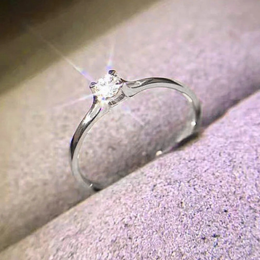 Ansoff Huitan minimalist women's wedding ring with 4mm cubic zirconia, simple elegant engagement band on a female finger.
