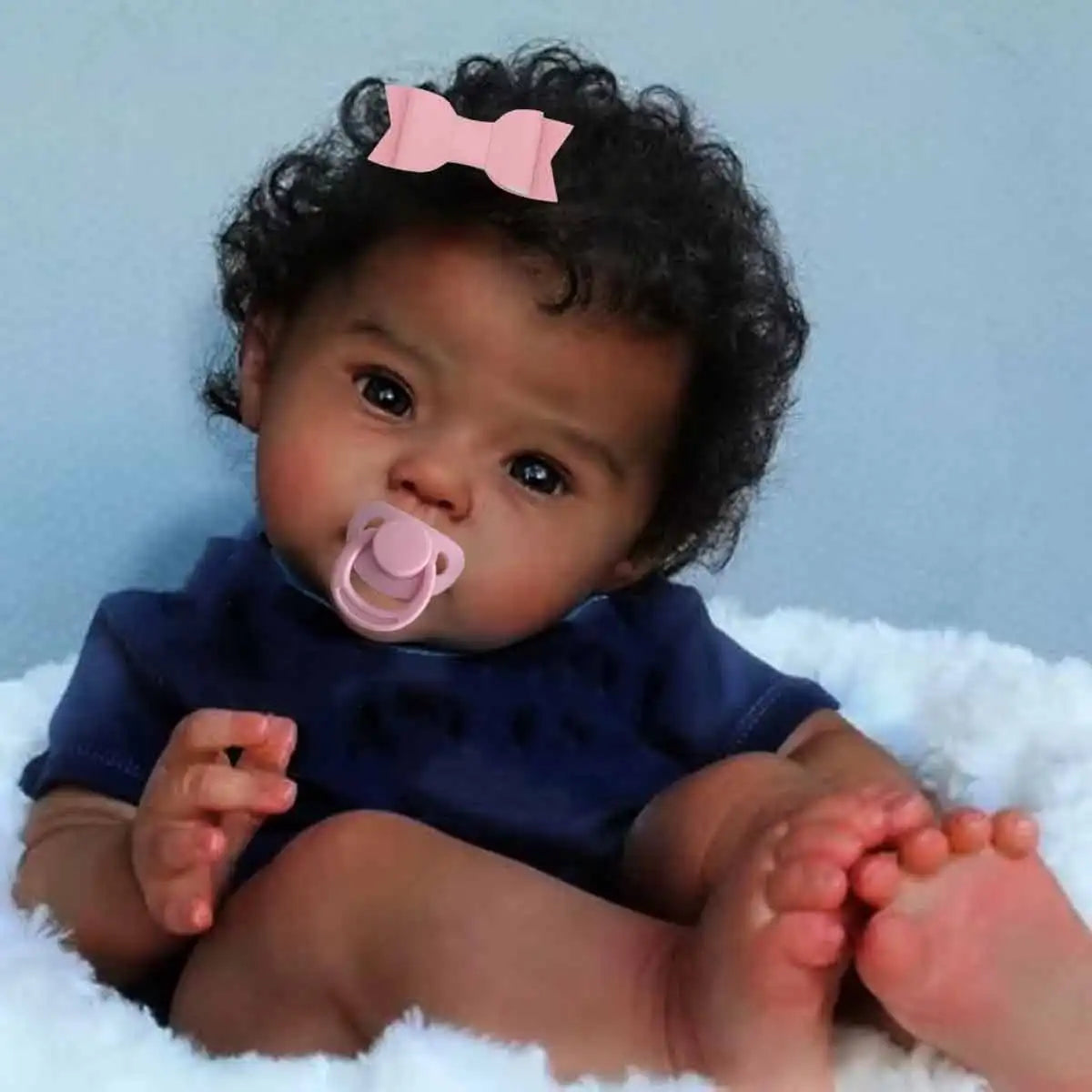 Realistic black reborn baby doll with soft cloth body, curly hair, and lifelike features by Ansoff.