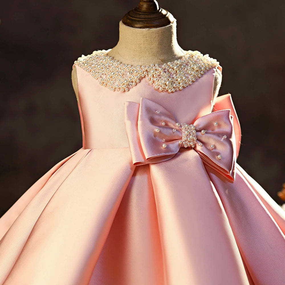 Pink satin princess gown for girls with glitter pearls, sleeveless design, and a pink bow, ideal for school performances and catwalk shows.